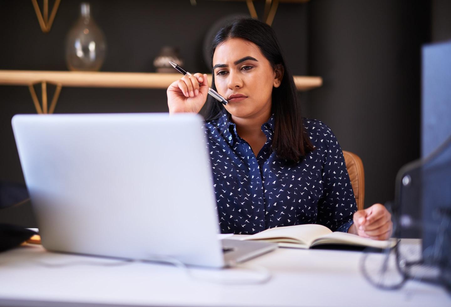 Focused businesswoman writing in a notebook while working alone on a laptop