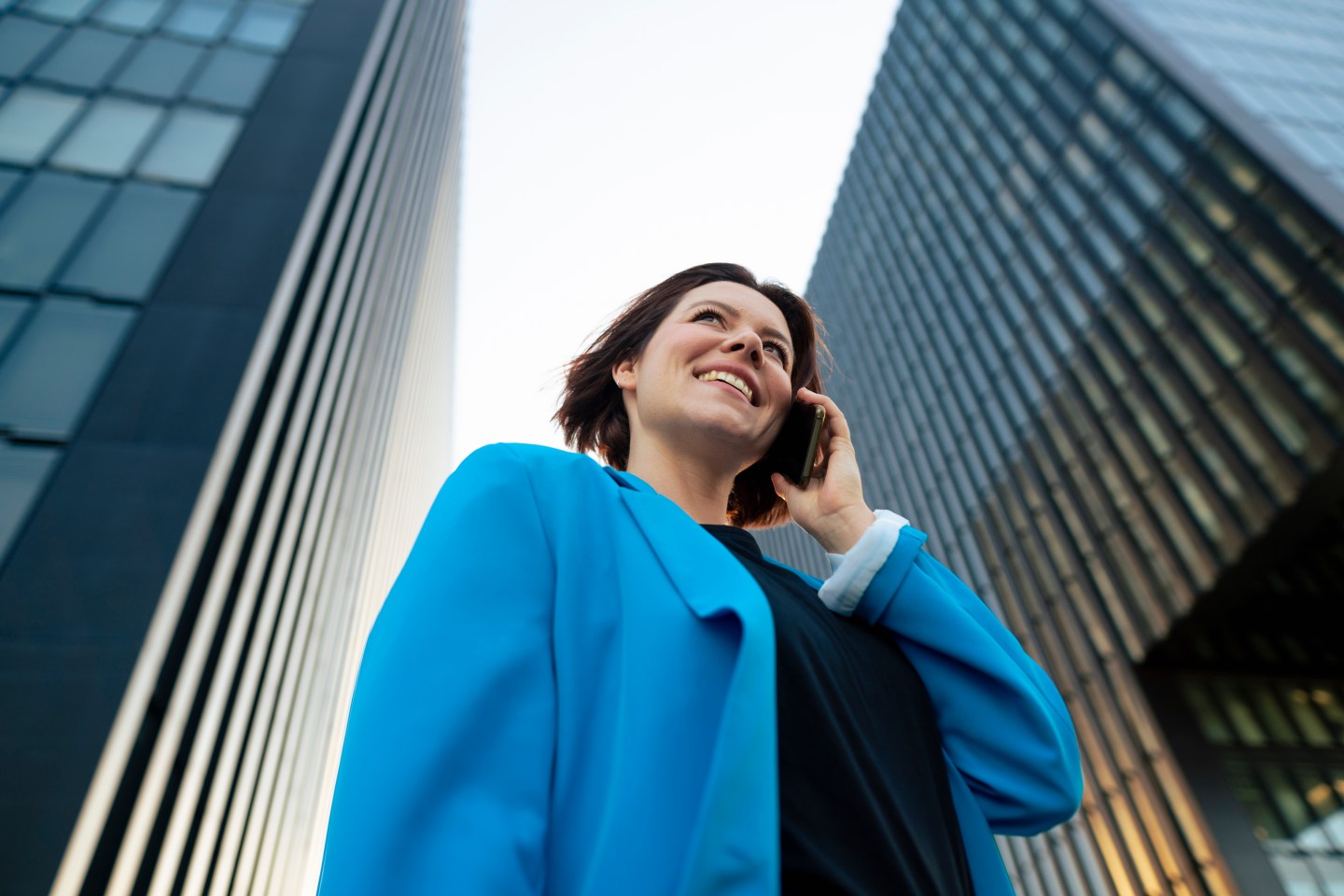 Happy businesswoman talking on mobile phone standing by office building