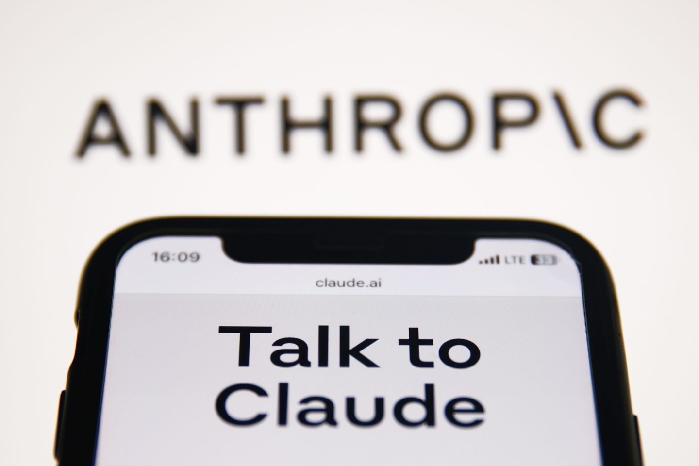 Anthropic Claude website displayed on a phone screen and Anthropic logo displayed on a screen in the background are seen in this illustration photo taken in Krakow, Poland on September 26, 2023.