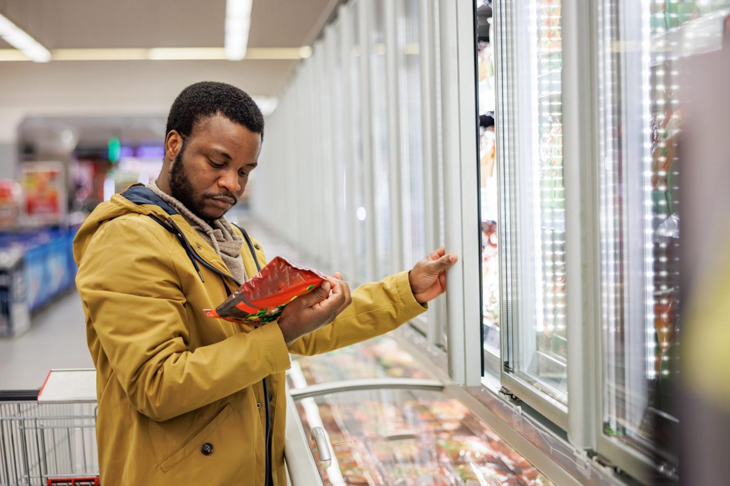 A man looks at a package in the freezer aisle of a grocery store.