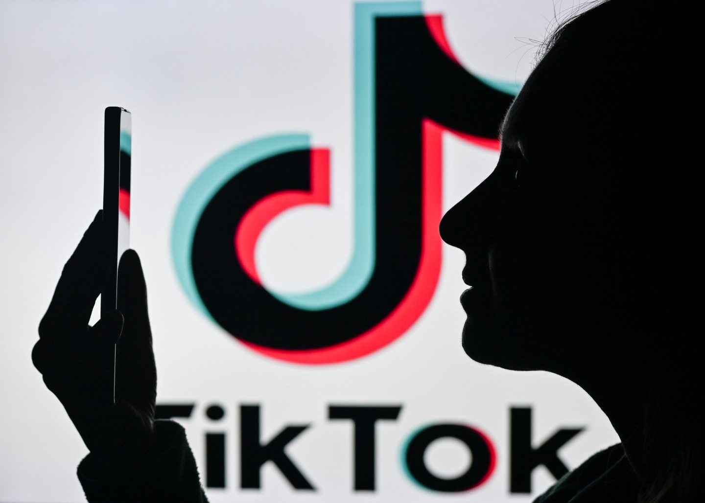 A woman holding a cell phone in front of the Tik Tok logo displayed on a computer screen, on April 29, 2024, in Edmonton, Canada.