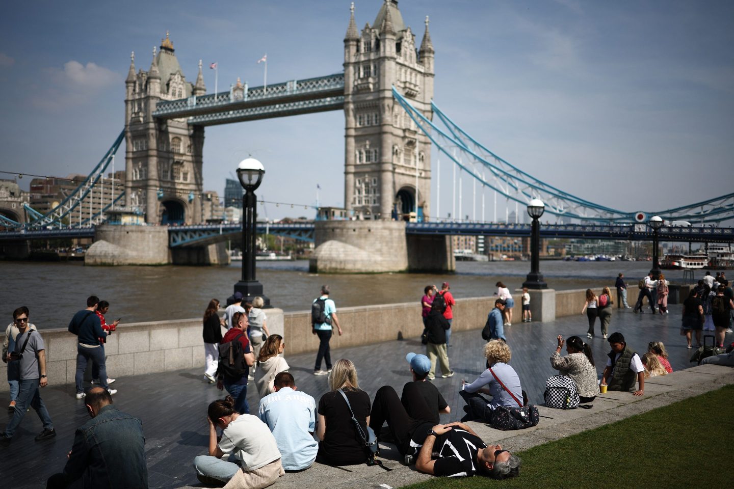 A person rests on the grass near the banks of the River Thames, backdropped by Tower Bridge in London,