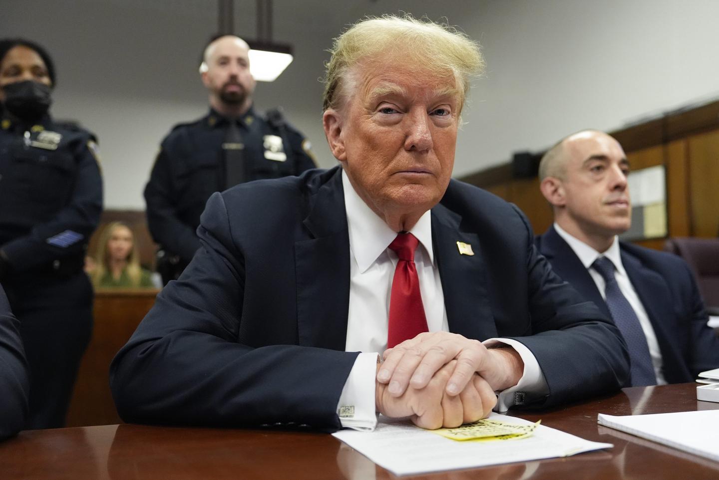 Donald Trump sits in a court room and looks directly at the camera.
