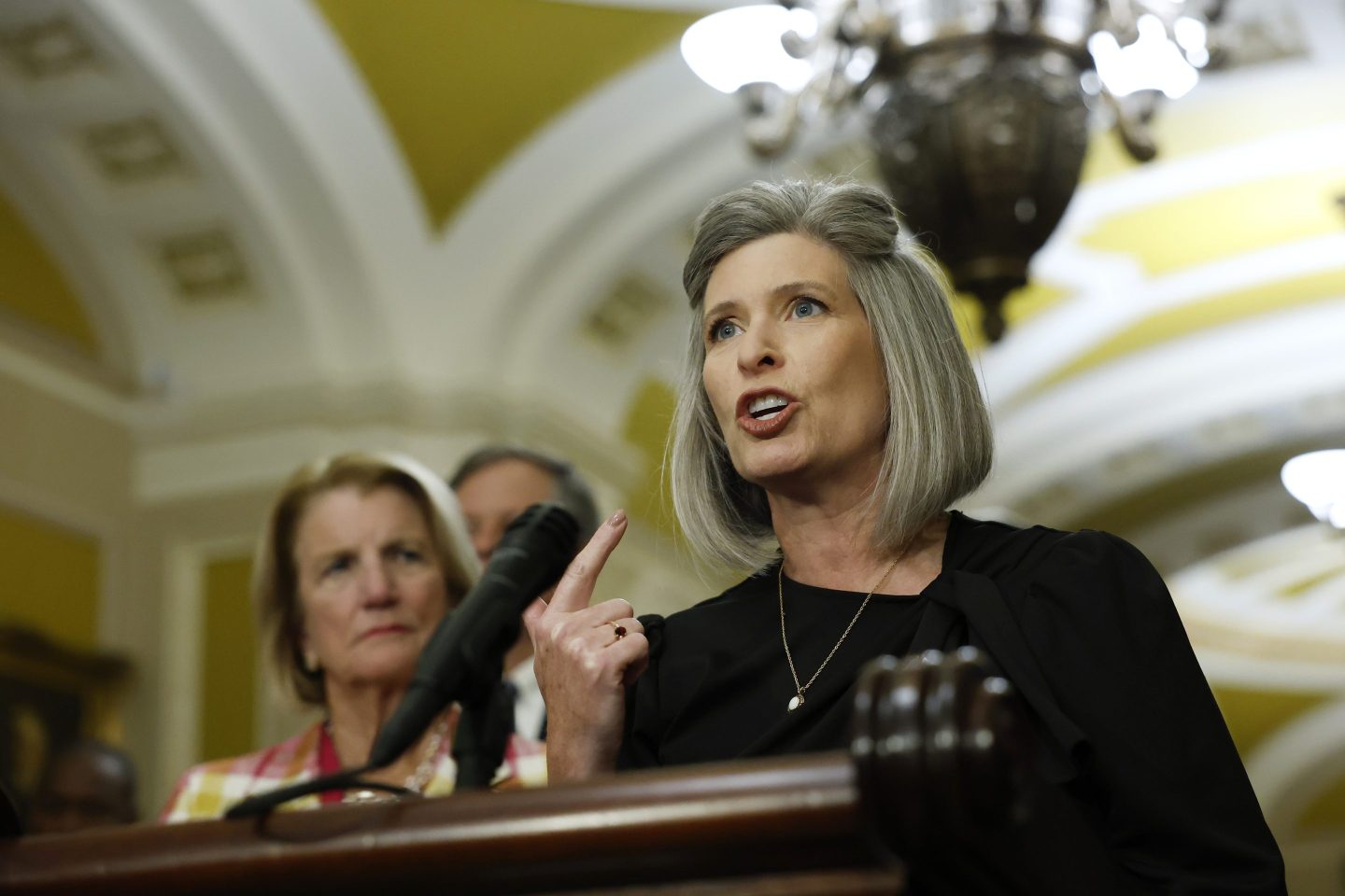 Sen. Joni Ernst (R-IA) points with her right index finger upwards as she speaks at a podium.