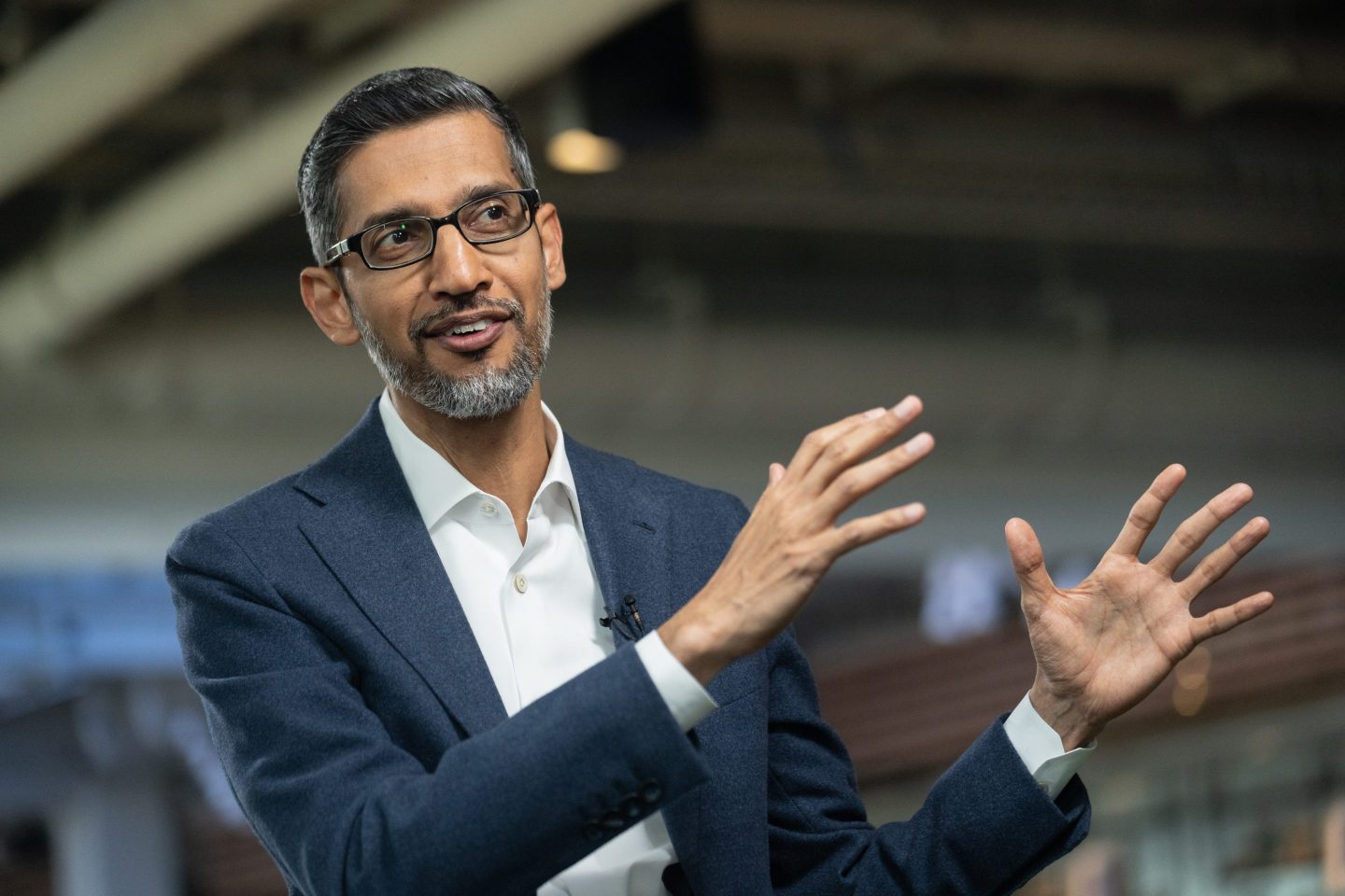 Sundar Pichai gestures with both hands to his left.