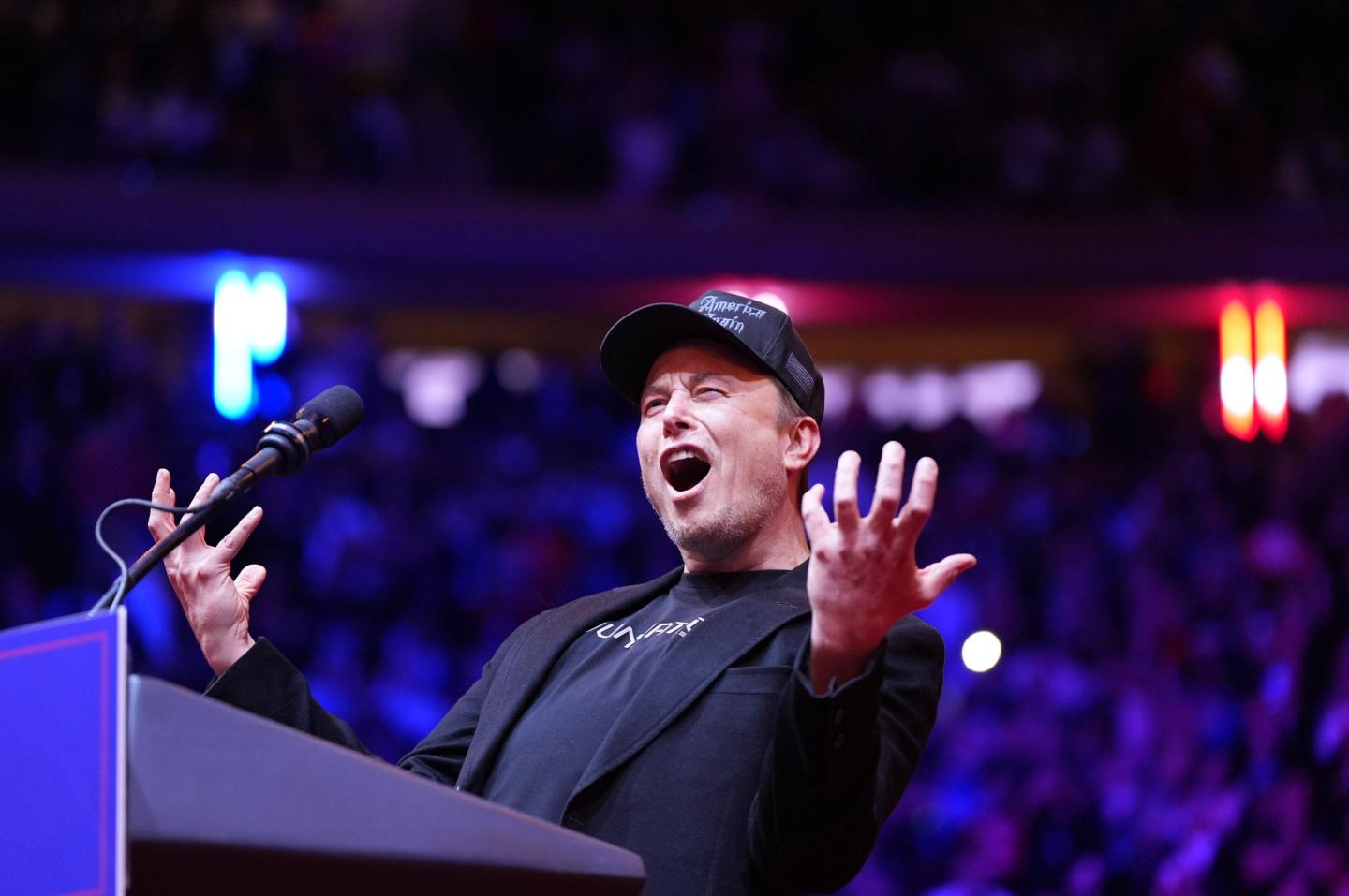 Elon Musk reaches out both of his hands and looks excited as he speaks on stage at a rally for Donald Trump at Madison Square Garden.