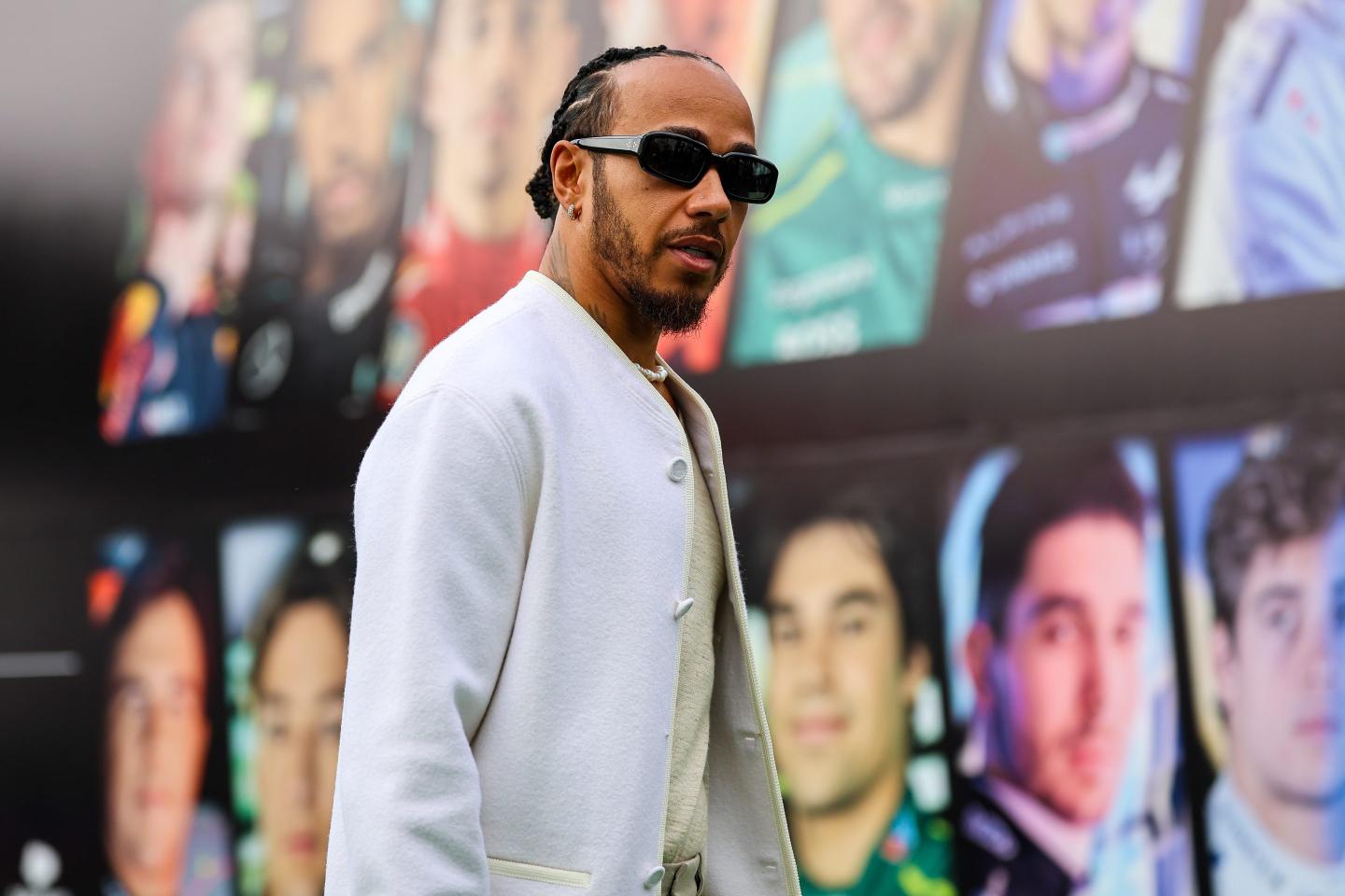 Lewis Hamilton in a white jacket and glasses in the F1 paddock