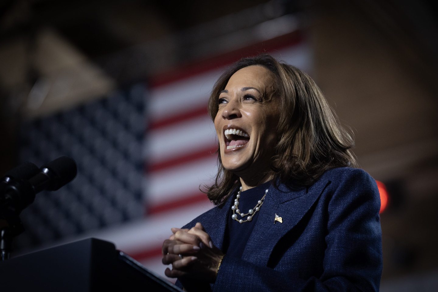 Kamala Harris smiles at a podium in front of the American Flag.