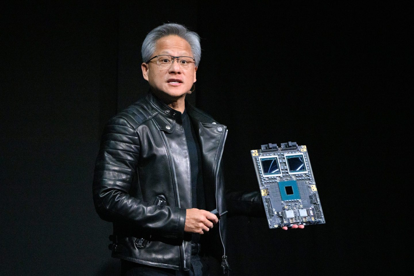 Jensen Huang holds up a circuit of Blackwell GPUs while speaking on stage.