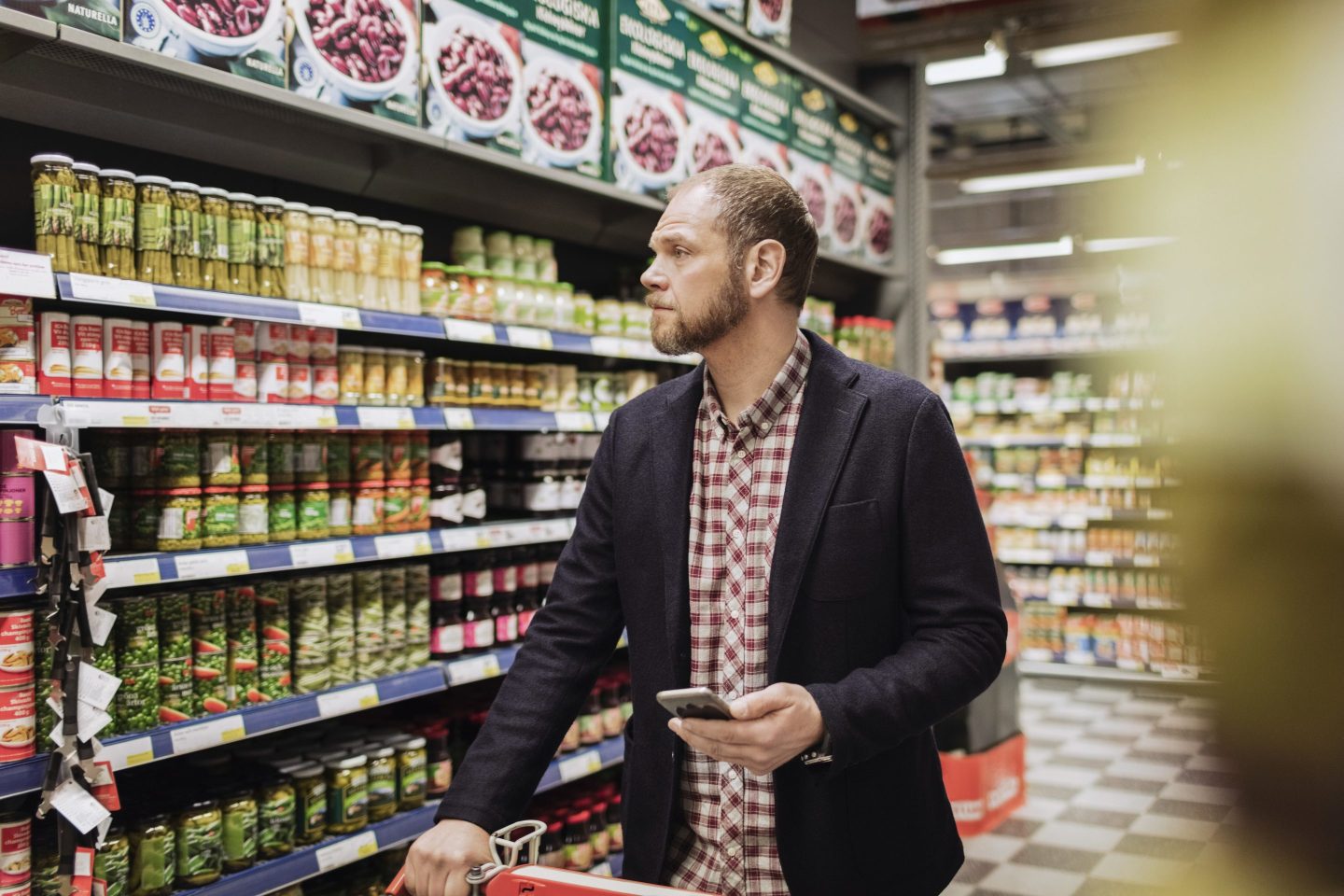 Man grocery shopping while looking up ingredients on his phone