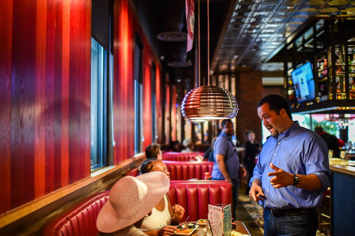 A man talks to customers sitting in a red TGI Fridays booth.