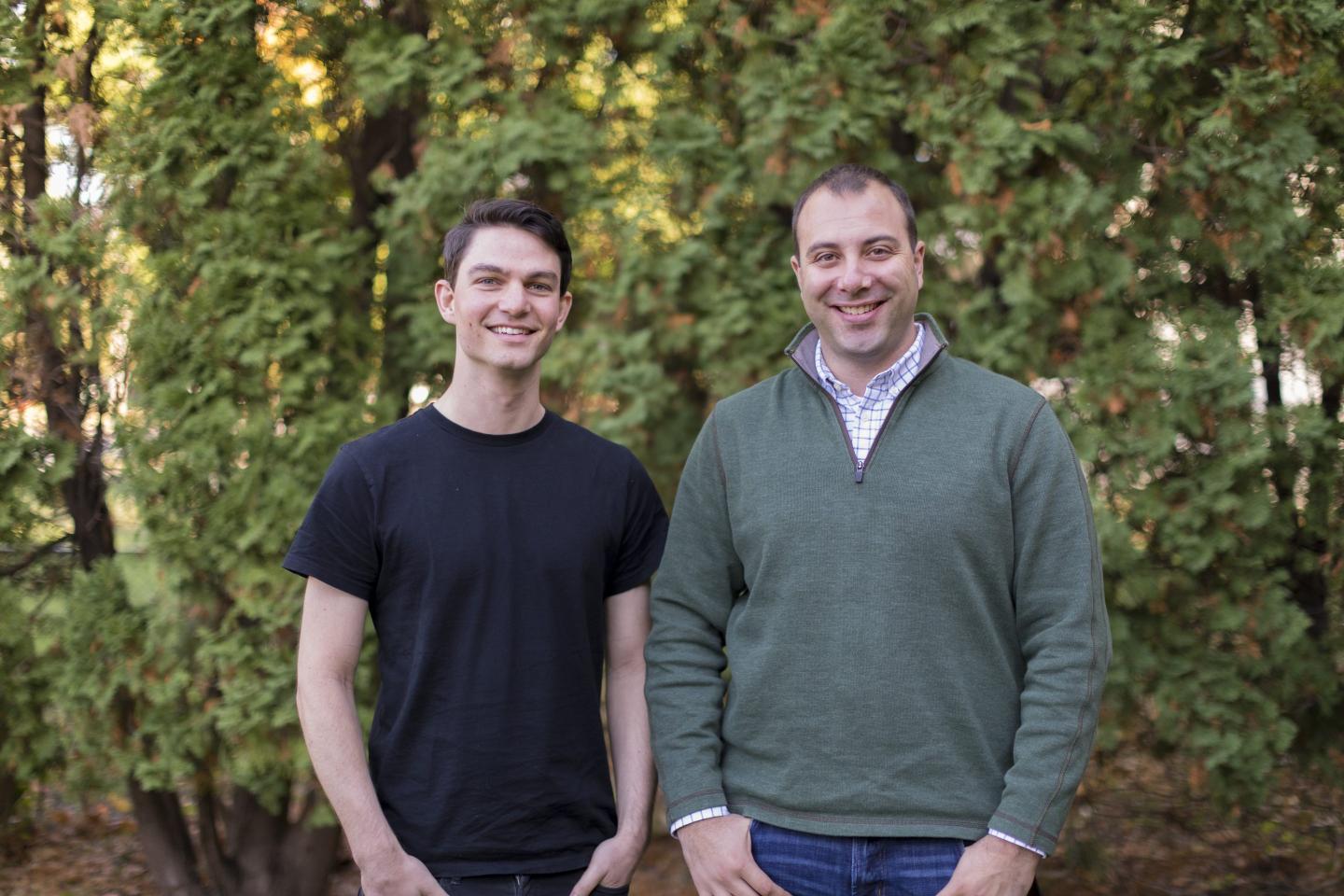 two men in casual clothing standing and smiling for a photo