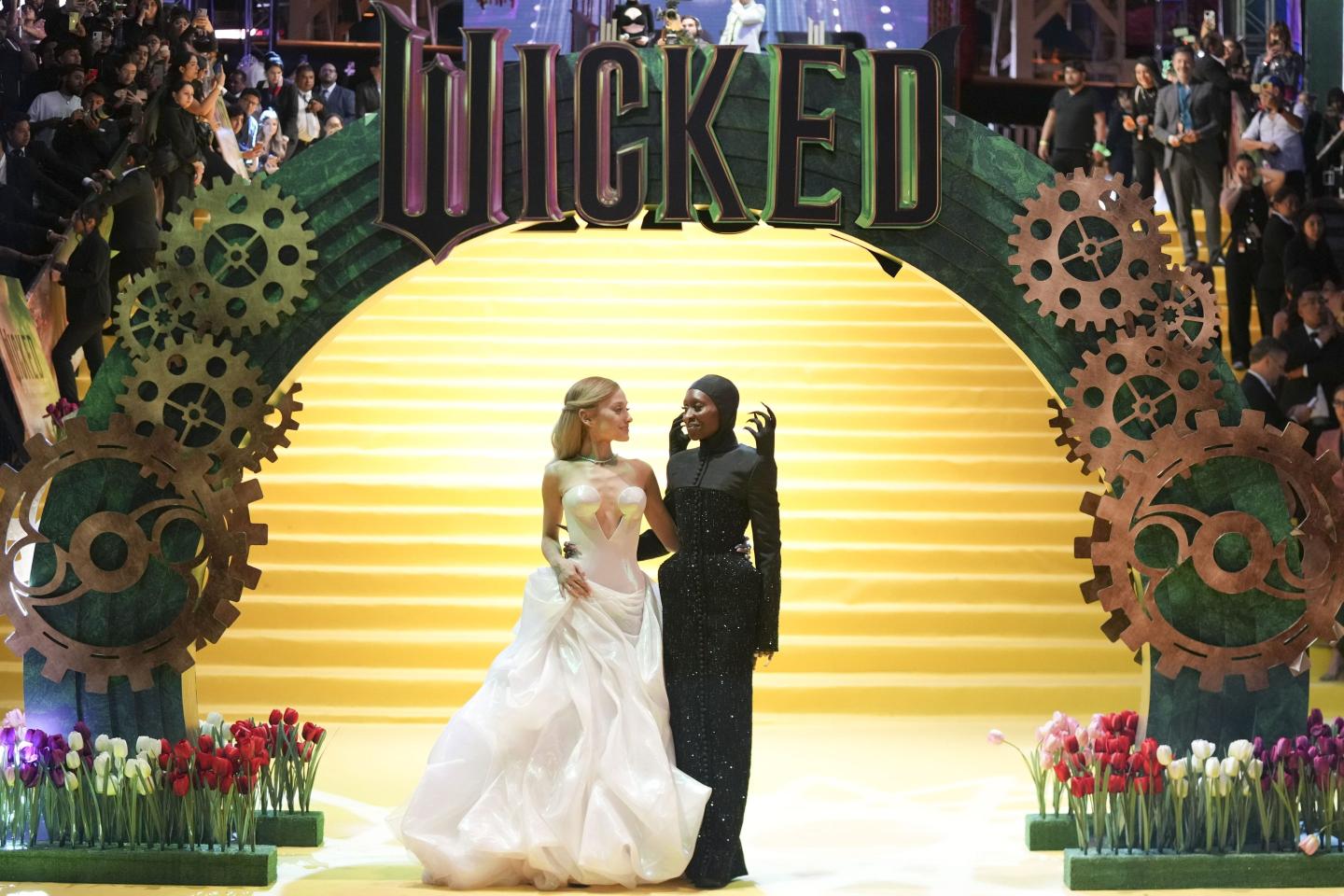 Ariana Grande and Cynthia Erivo stand in front of a Wicked display