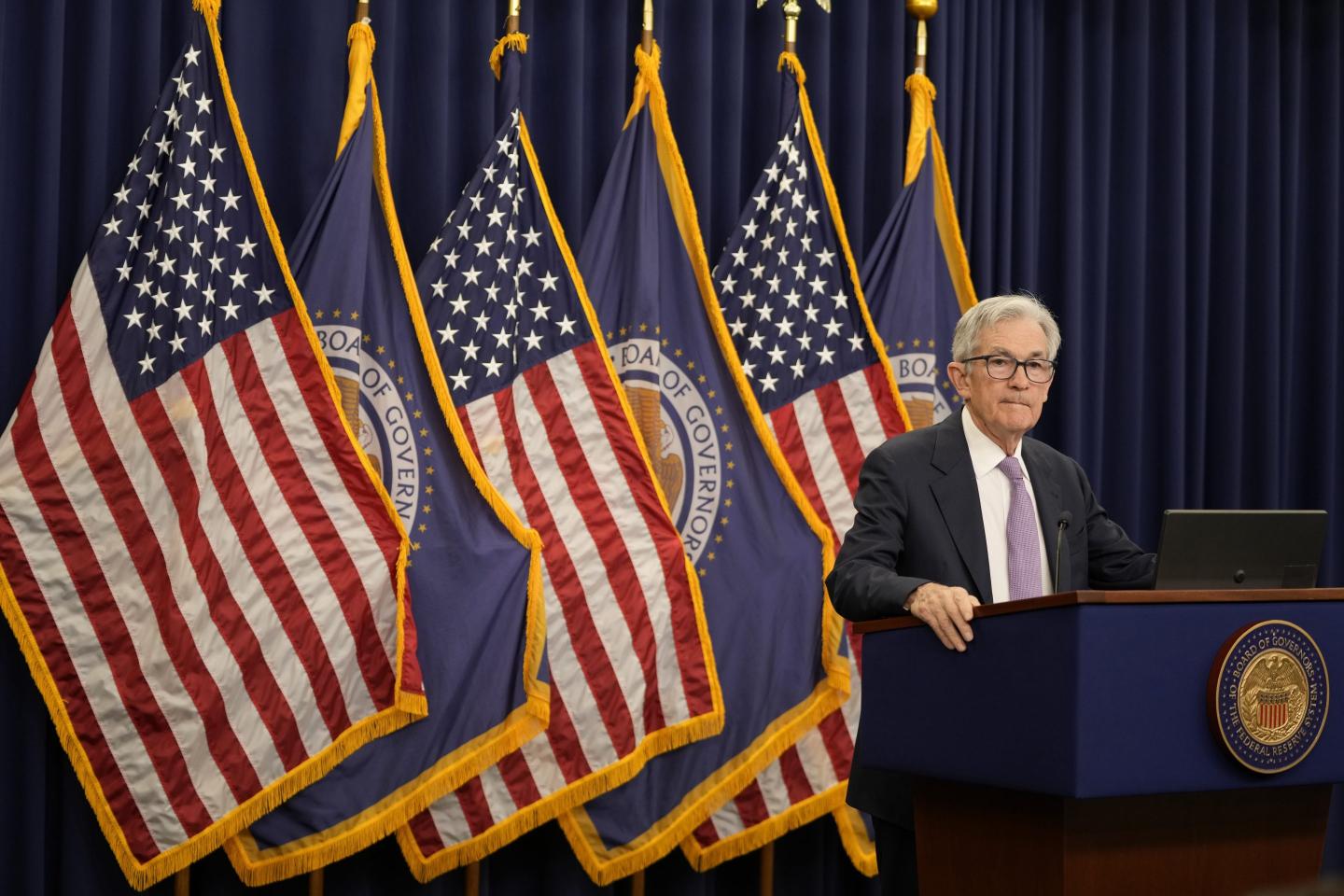Fed chairman Jay Powell stands at a podium in front of roughly six flags