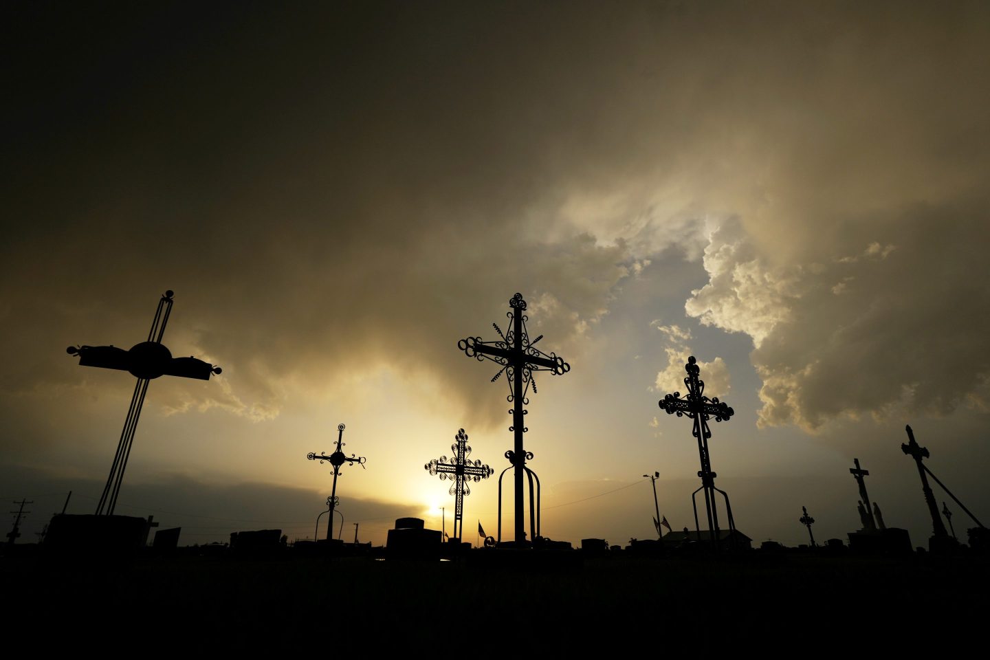 Iron crosses marking graves are silhouetted against storm clouds building over a cemetery on May 25, 2024, in Victoria, Kan.