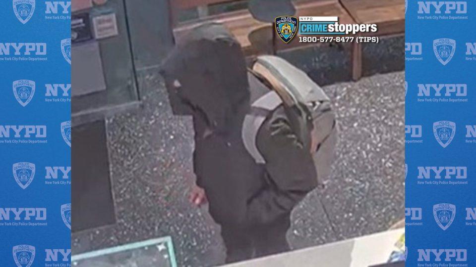 A survaillence image of a man in a dark hooded jacket wearing a gray backpack.