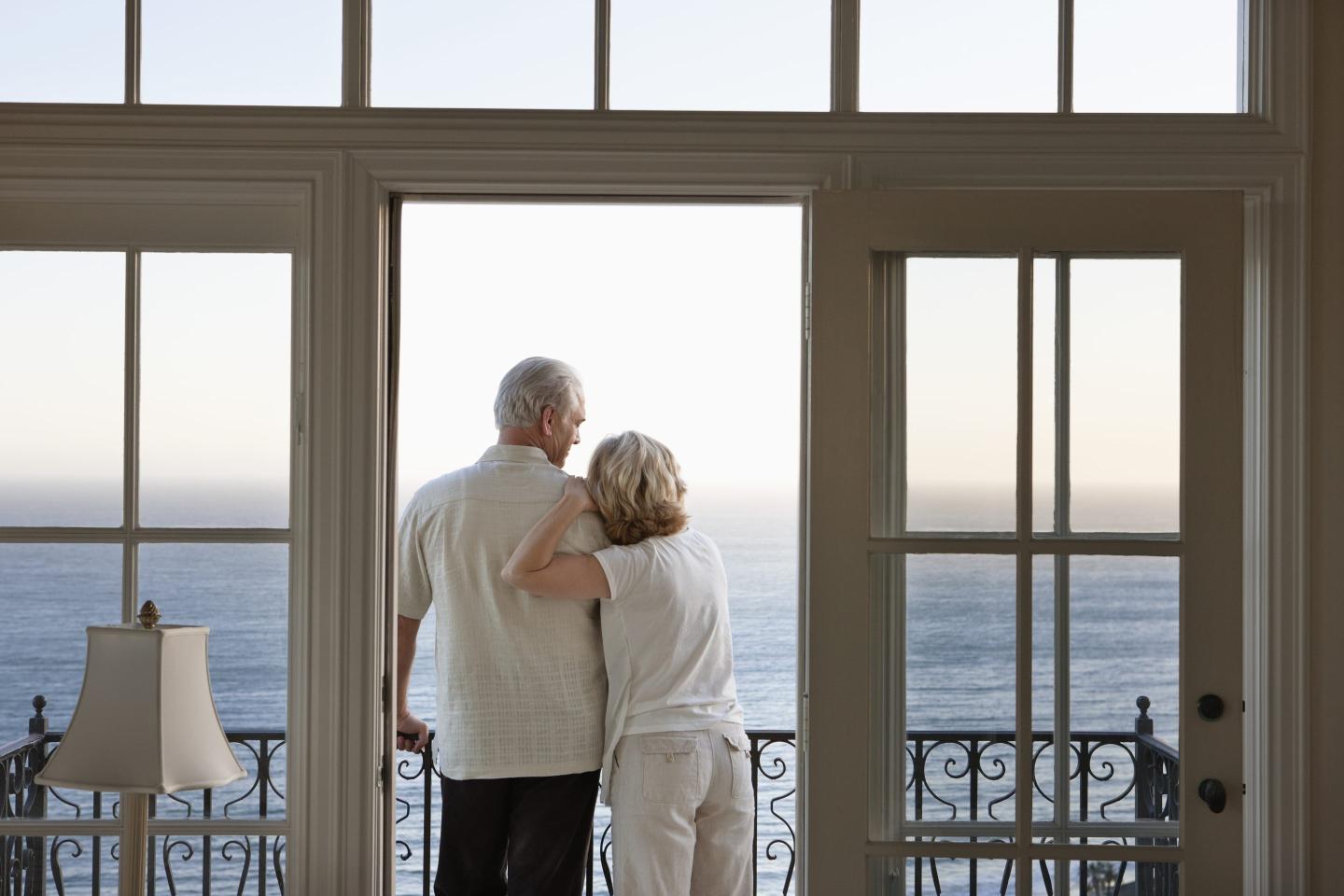 A boomer couple looking out of a hotel balcony window