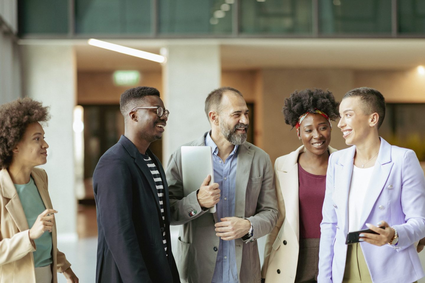 group of coworkers standing in an office corridor, chatting and smiling