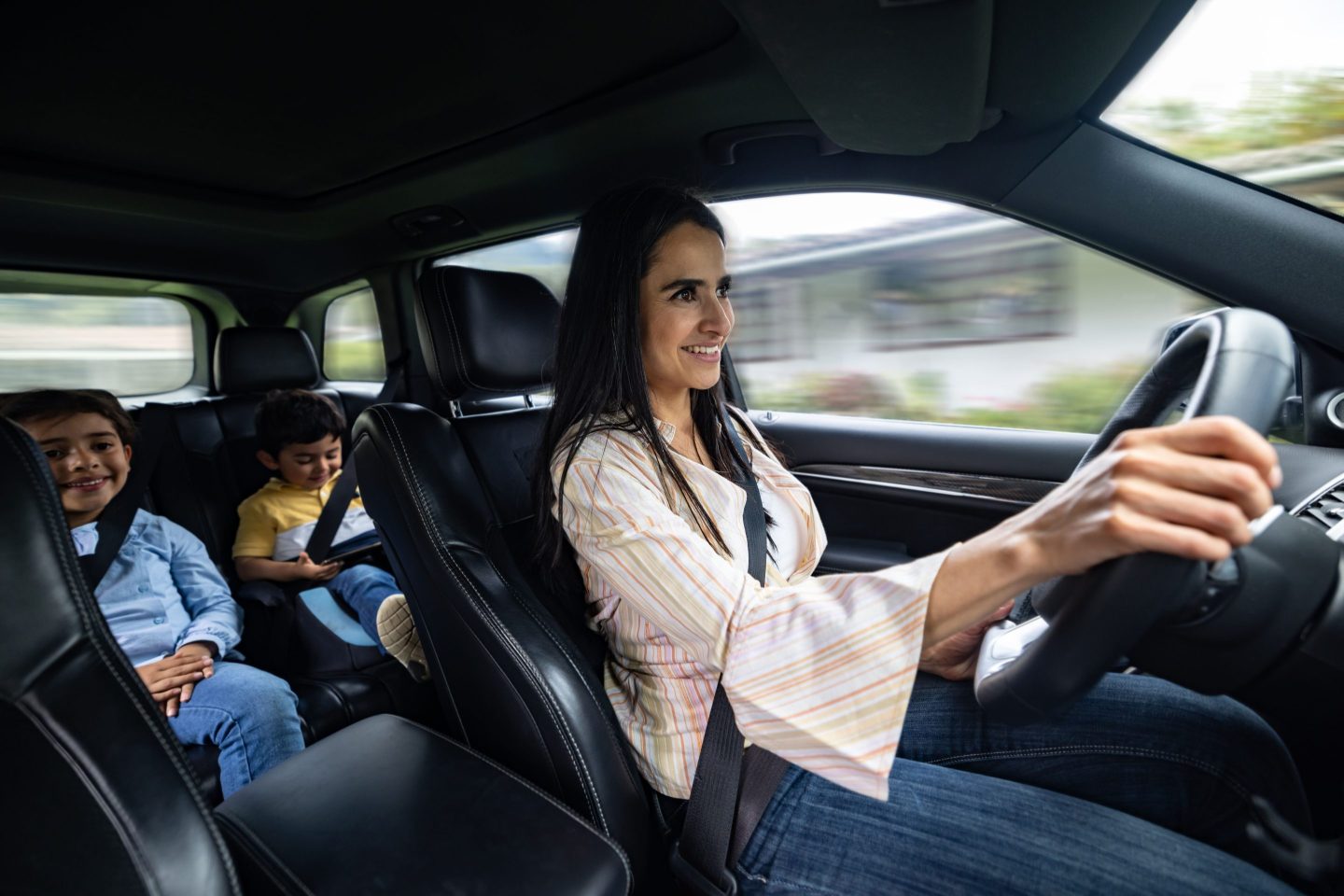 Happy Latin American mother driving her kids to school and smiling