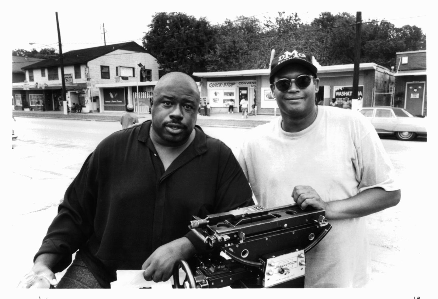 Two men stand over film equipment in the middle of the street.