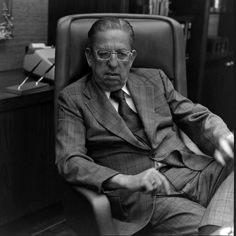 A man in a suit sits at an office desk.