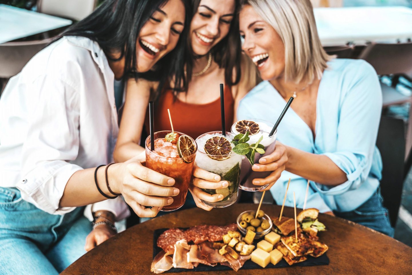 Three beautiful young women drinking mocktails sitting at bar restaurant table