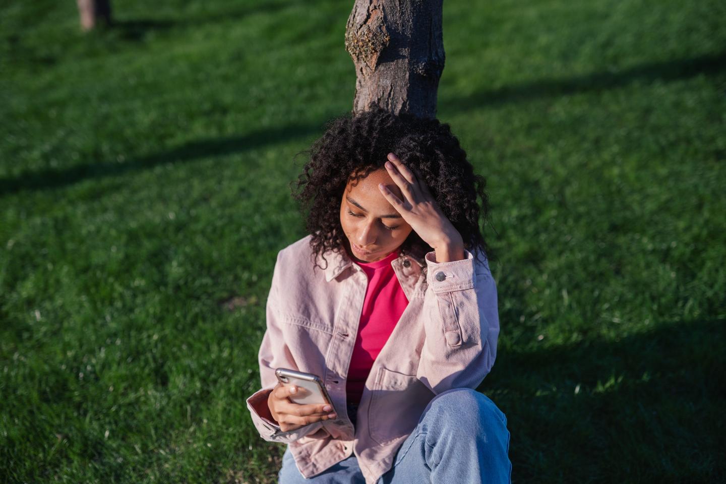 Woman scrolling on her phone sitting under a tree