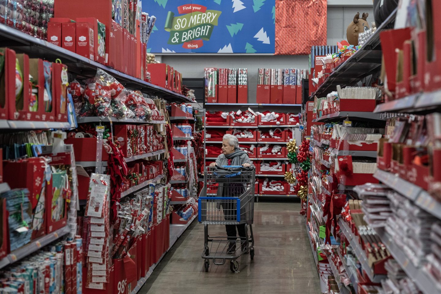 A woman pushes a cart through an aisle filled with Christmas-themed merchandise.
