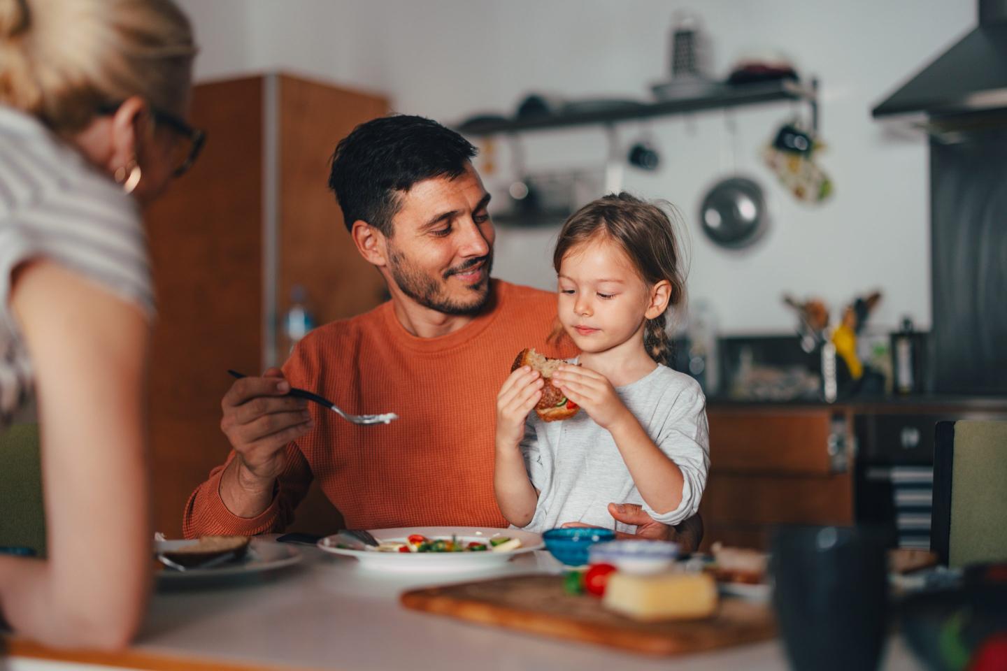 child and parents sit together eating breakfast
