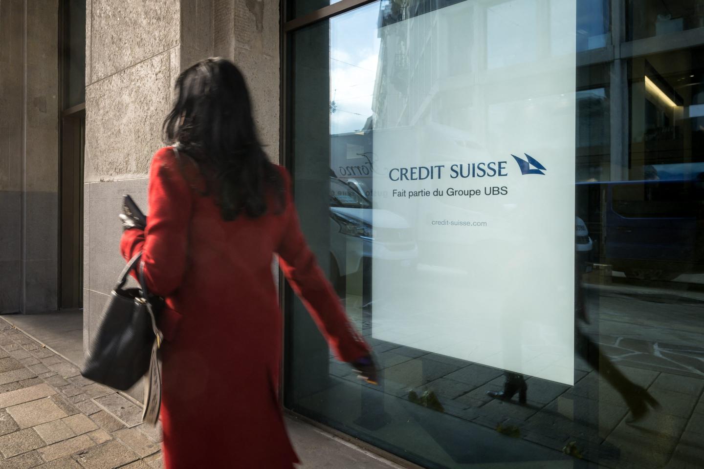 A woman walks past an advertising reading in French "Credit Suisse, part of UBS Group.
