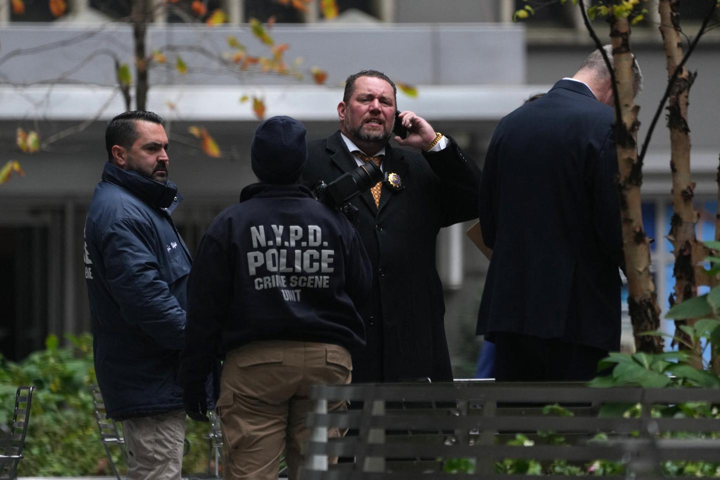 A group of people, including a person in an NYPD jacket, stand outside.