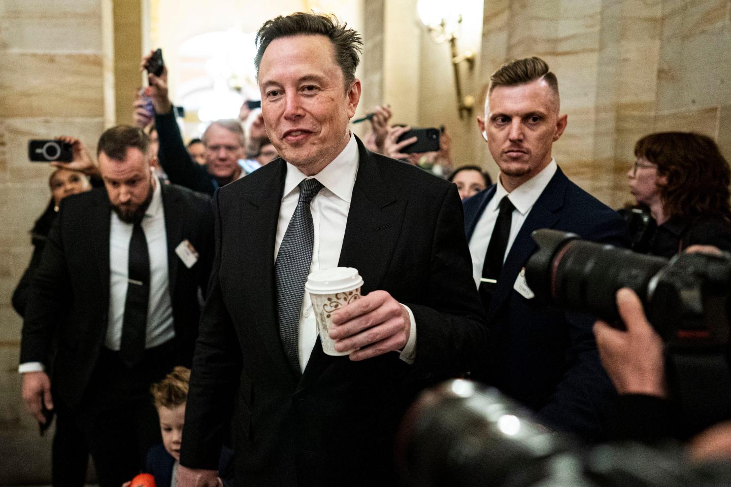 Elon Musk holding a coffee cup in a media scrum
