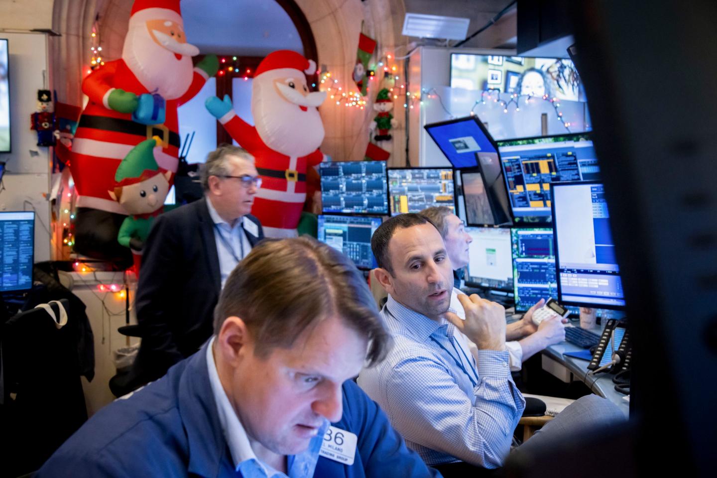 Traders on the floor of the New York Stock Exchange talk and look at their monitors with Christmas decorations in the background.