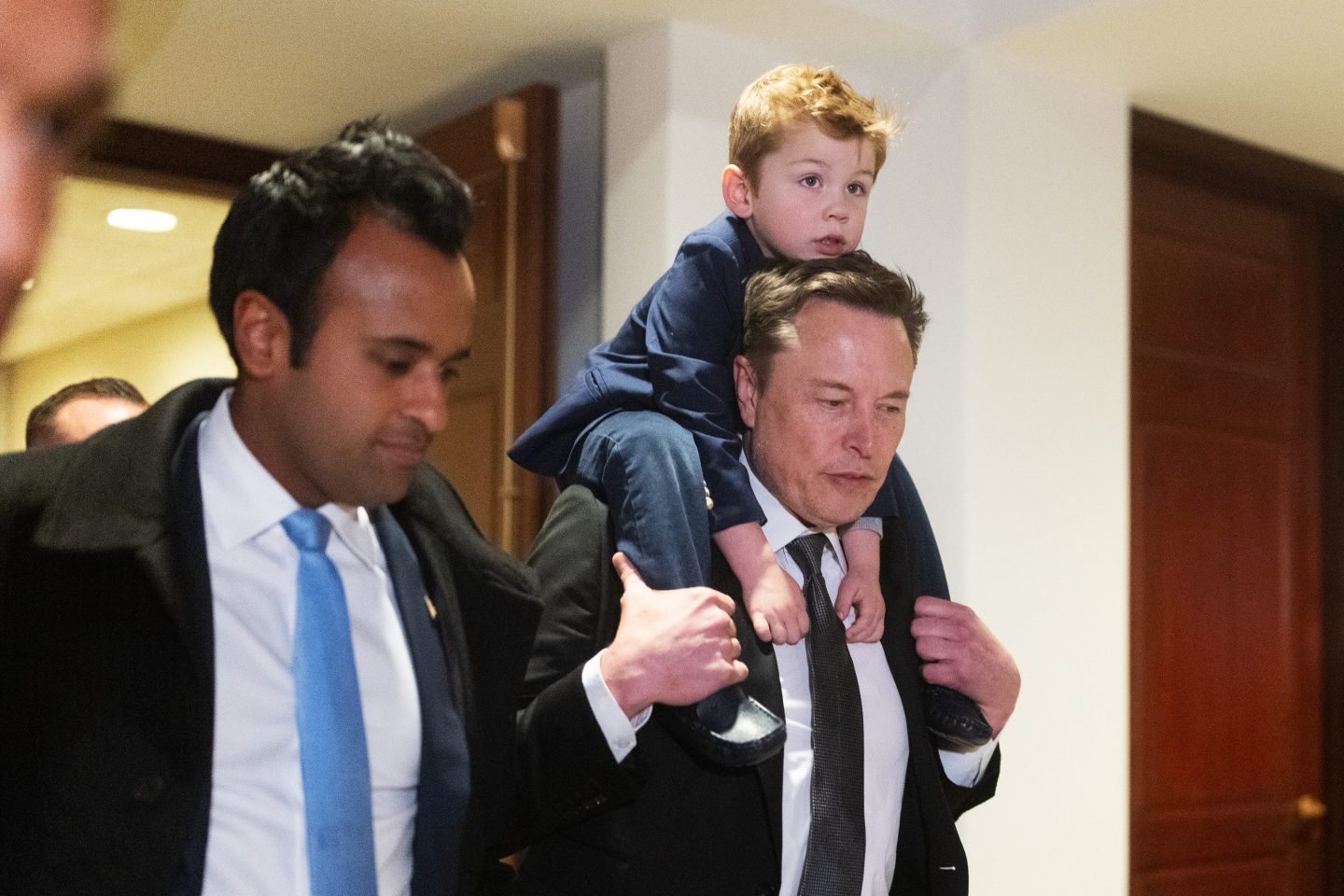 Vivek Ramaswamy walking next to Elon Musk, who is carrying a child on his shoulders.