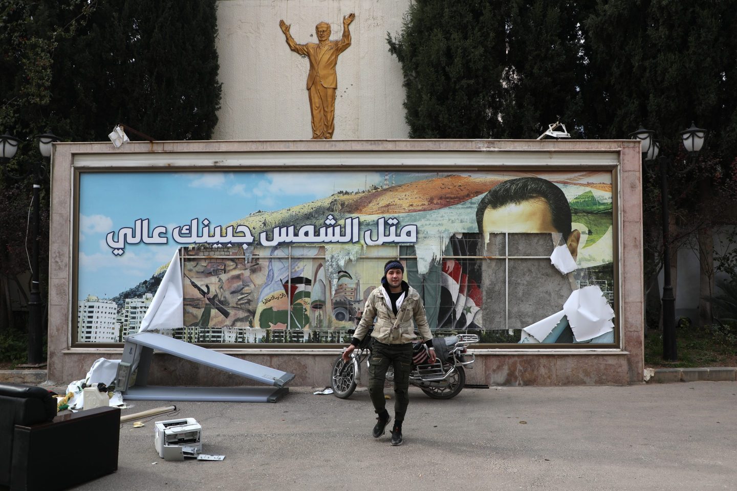 A man is pictured in front of a vandalized political banner featuring a portrait of Bashar al-Assad, following news the Syrian government regime had fallen on, Dec. 8, 2024 in Damascus.