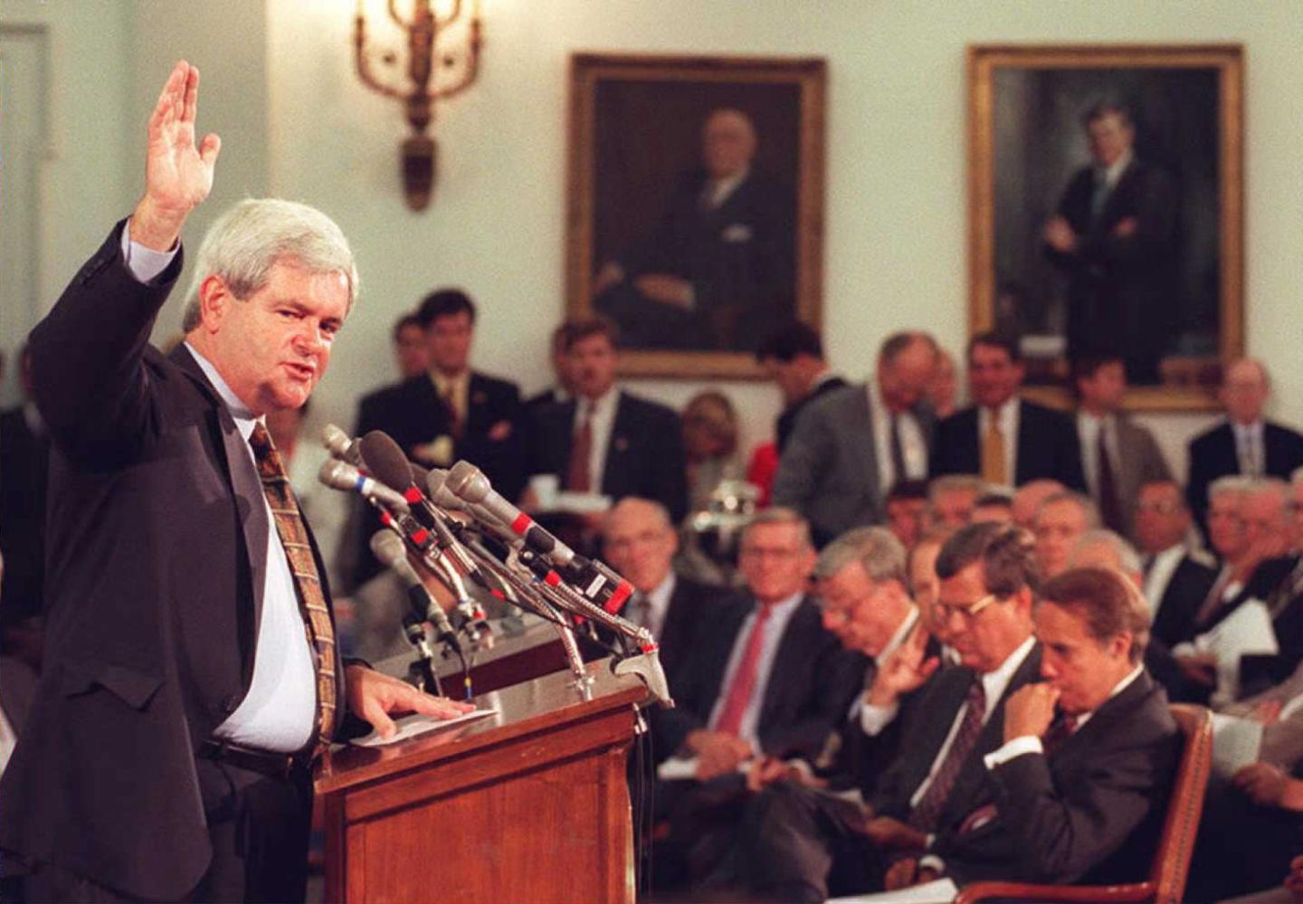 A politician speaks at a podium with microphones in front of an audience.