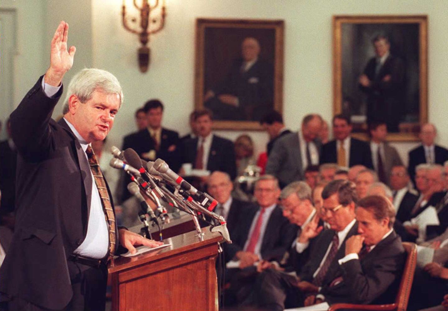 A politician speaks at a podium with microphones in front of an audience.