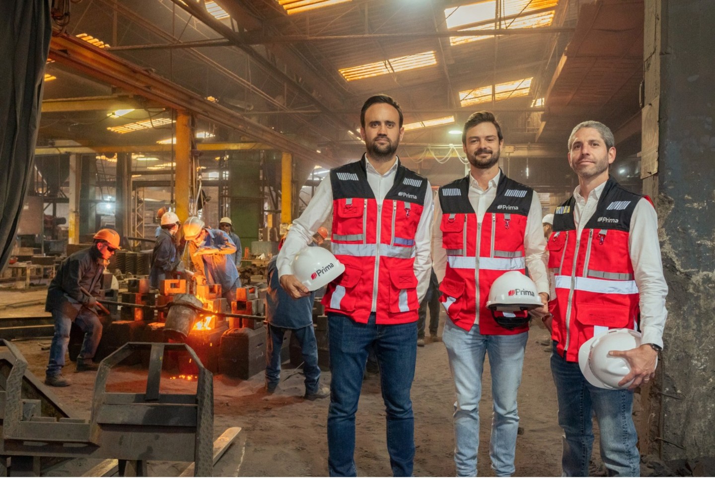 3 men wearing vests and holding hard hats pose for a photo