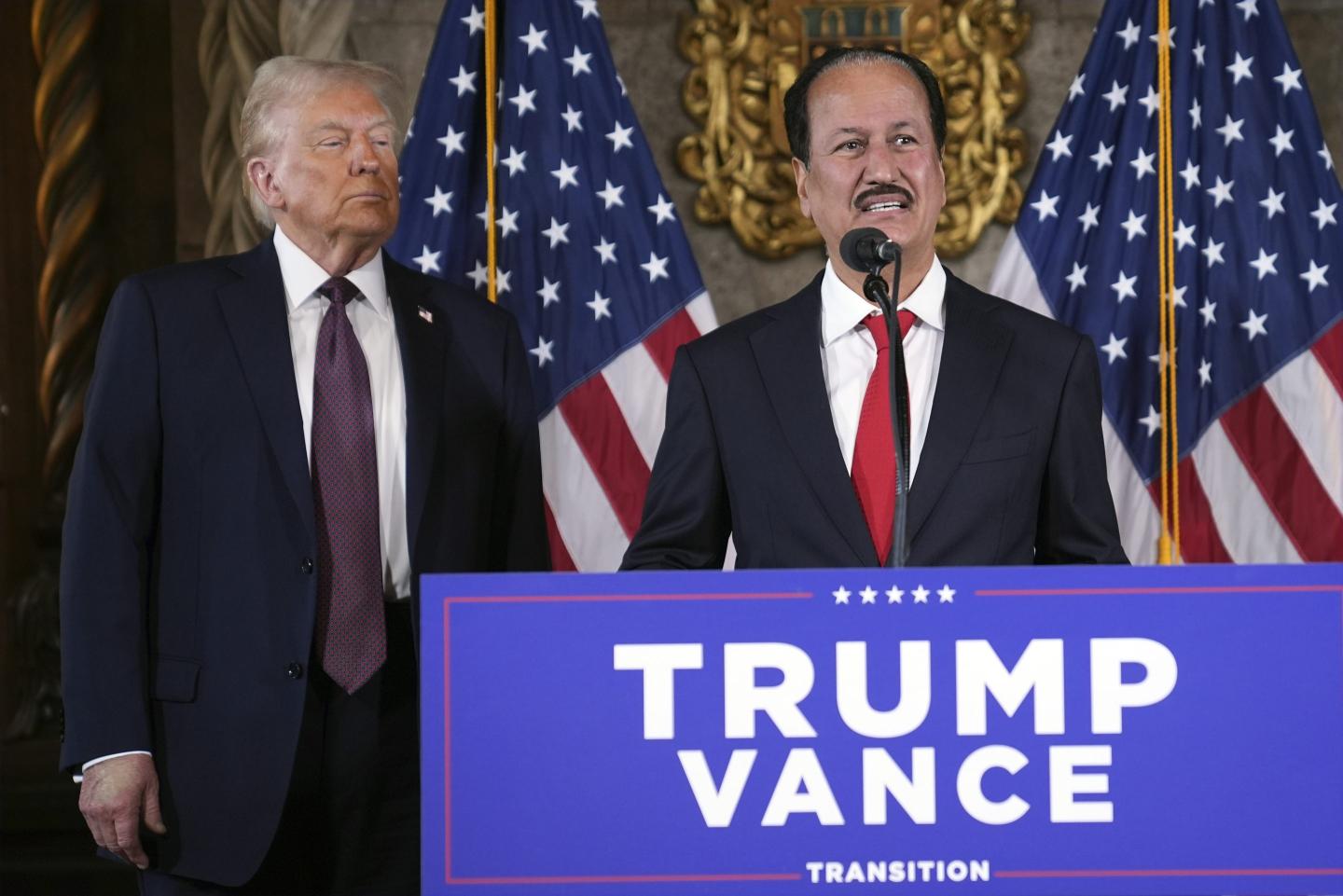 Donald Trump looks on as Dubai billionaire Hussain Sajwani stands at a podium and speaks into a microphone