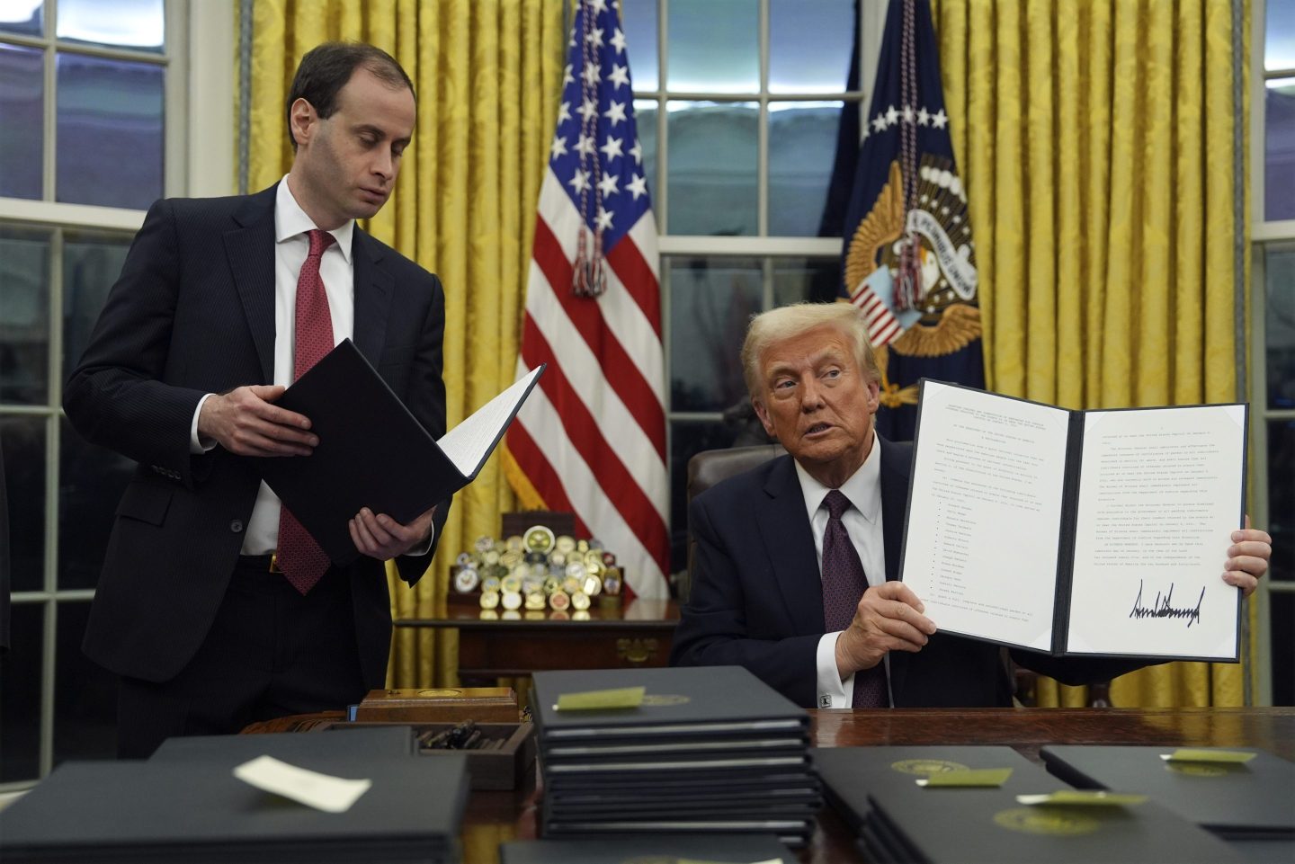 President Donald Trump holds up an executive order commuting sentences for people convicted of Jan. 6 offenses in the Oval Office of the White House, on Jan. 20, 2025, in Washington.