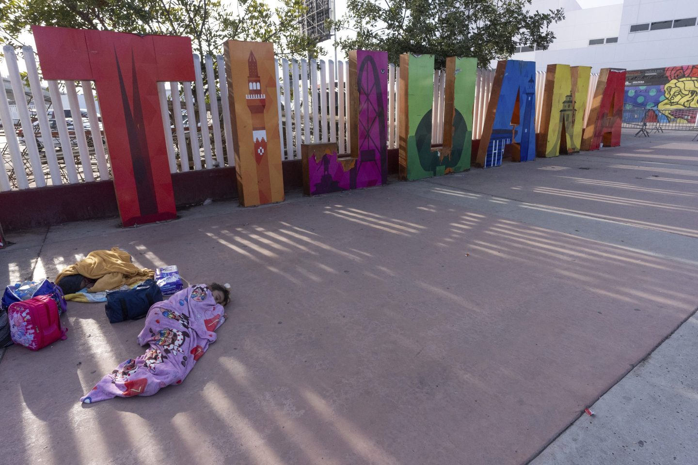 A girl from the Mexican state of Morelia sleeps in front of a sign for Tijuana as her family's CBP One application appointments to apply for asylum in the U.S. were declared not valid on the application on Jan. 20, 2025, in Tijuana, Mexico, shortly after President Donald Trump was sworn-in.