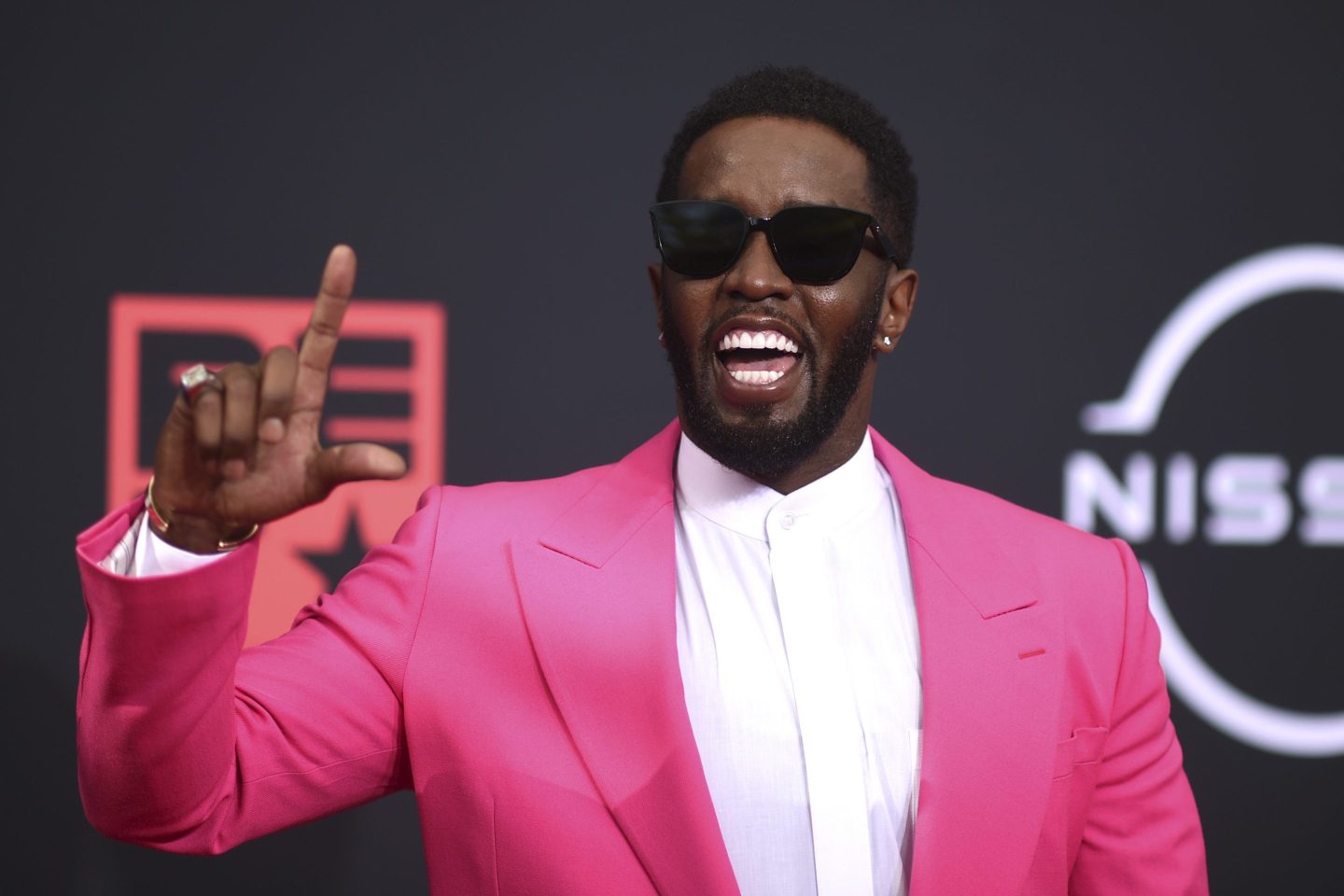 Sean Diddy Combs wearing sunglasses and a pink suit holding up his finger