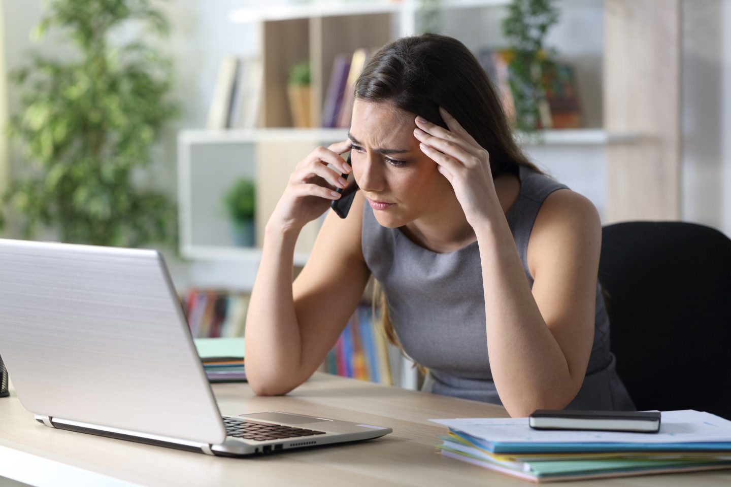 Worried entrepreneur calls on phone with laptop at home office.