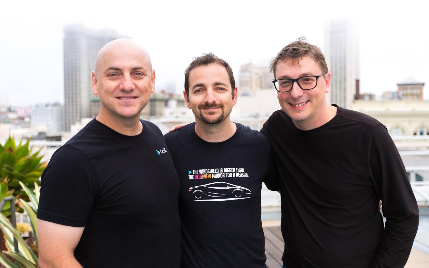 three men in black t-shirts smile for a photo
