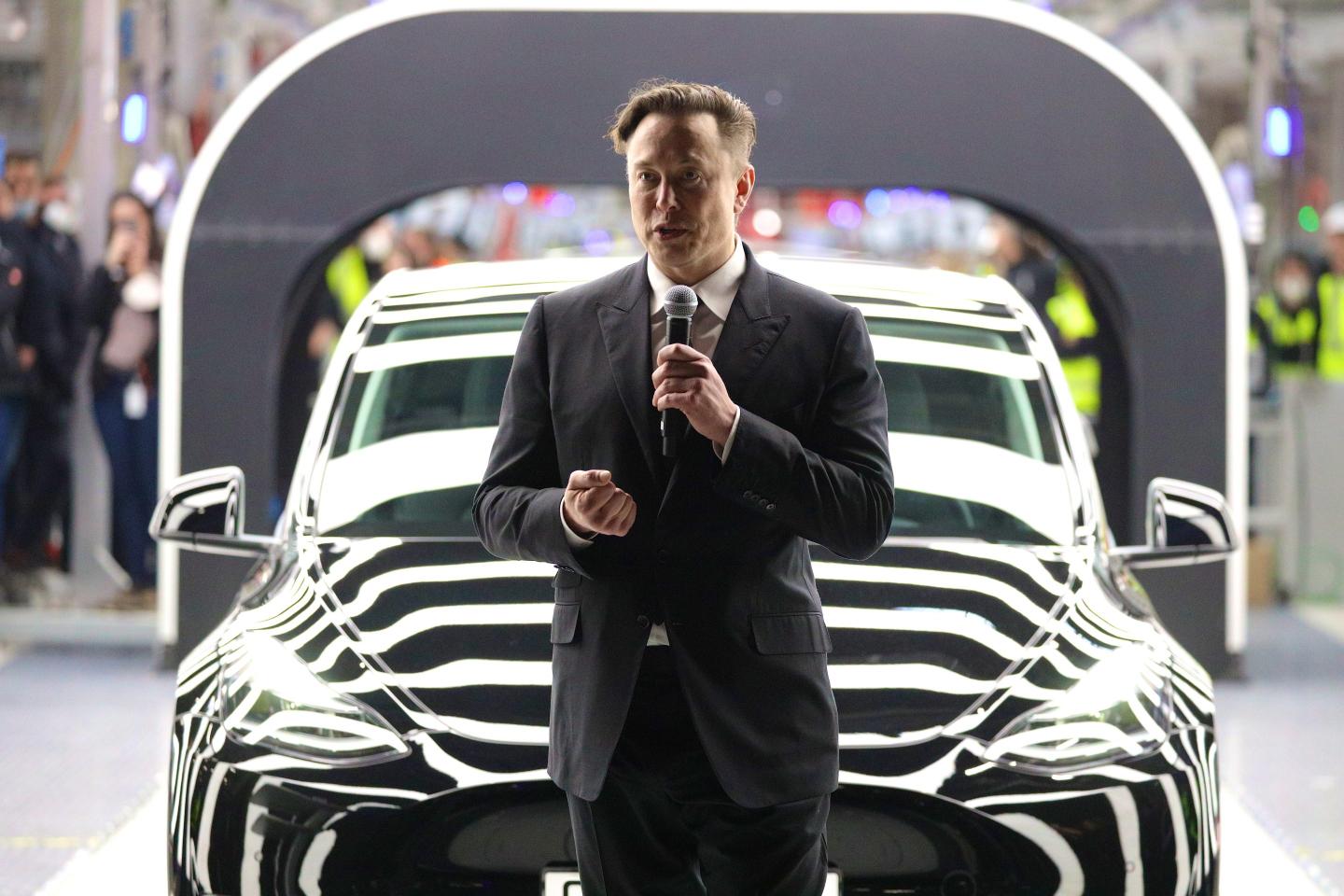 Tesla CEO Elon Musk speaking in front of a black Tesla
