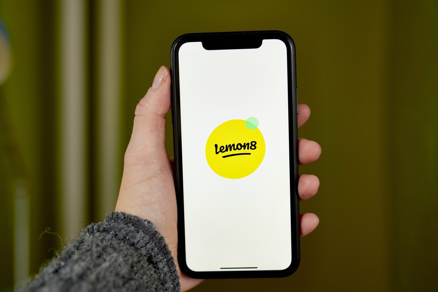 A hand holding a phone with the Lemon8 logo on it
