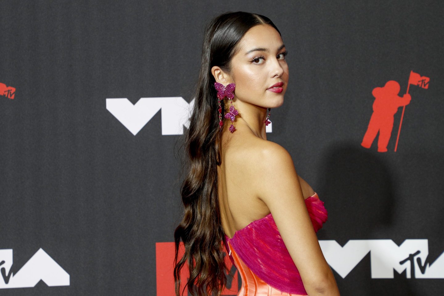 Olivia Rodrigo turns to face the camera wearing a pink dress and long pink earrings