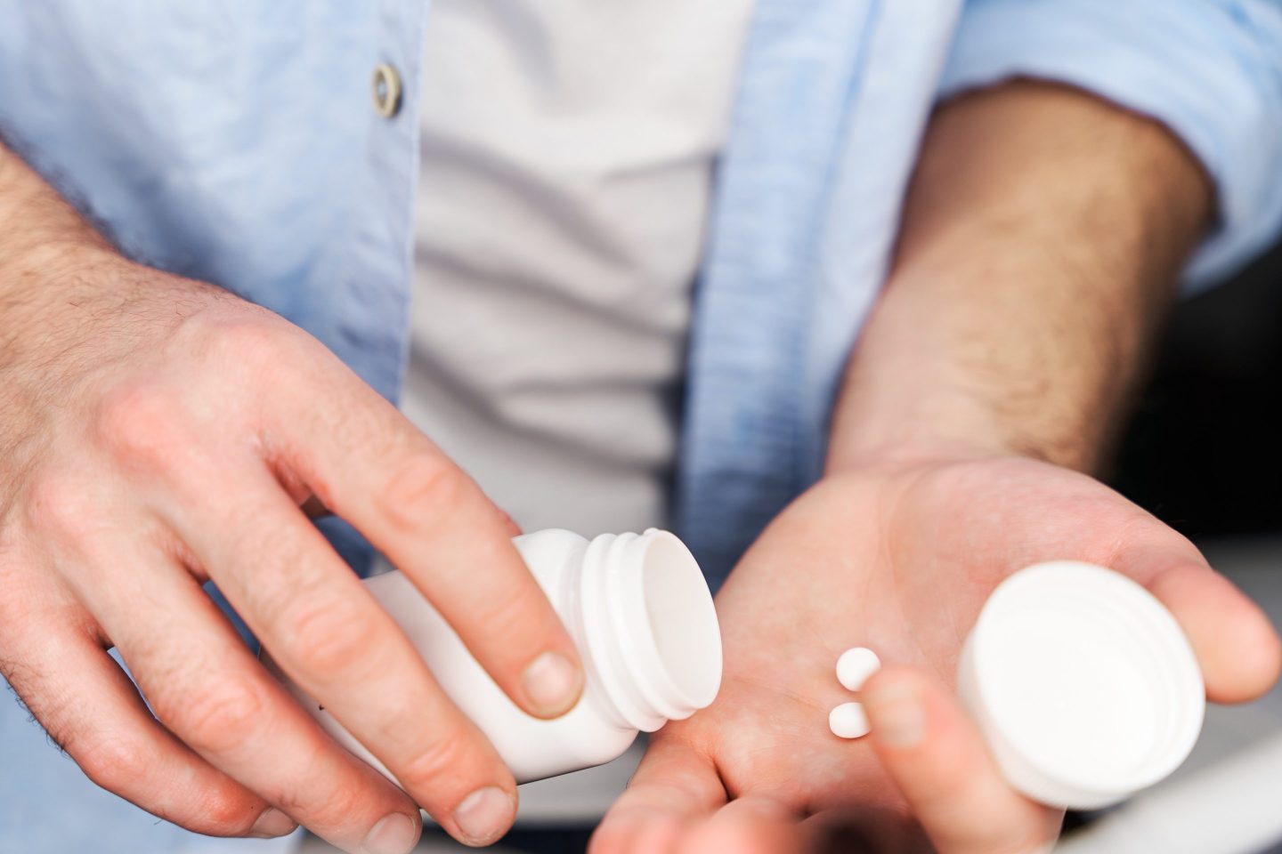 Close-up view of man in blue button-down shirt placing pills in his hand.