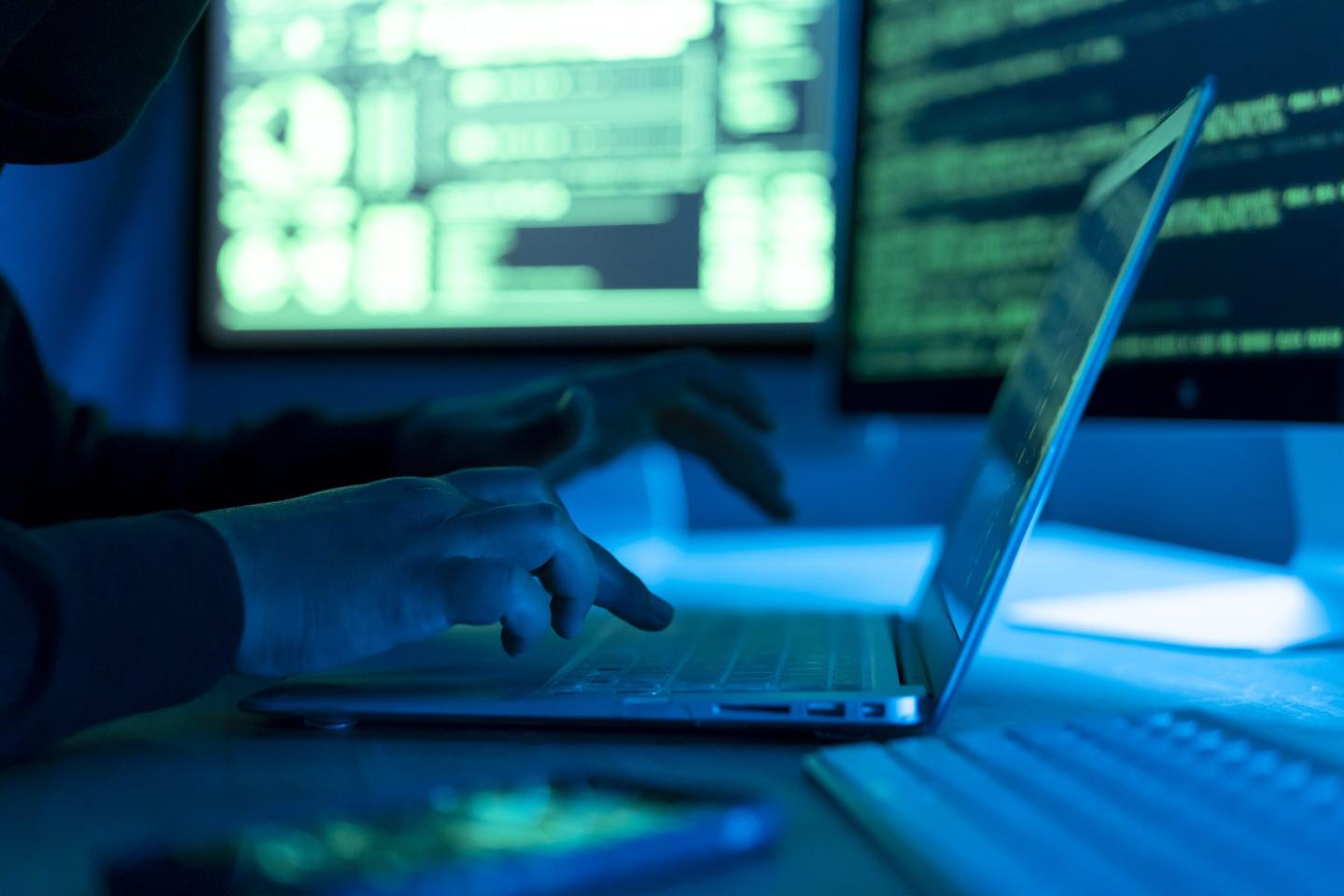 Close up of hands on a laptop in the dark with glowing green screens in the background
