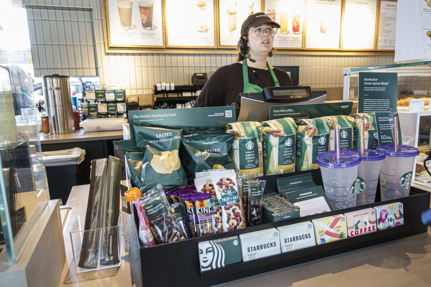 A Starbucks barista with a concerned look on her face stands behind a register.